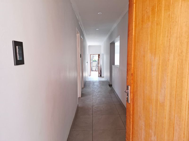 A clean, well-lit hallway featuring neutral tiled flooring and recessed lighting, providing access to multiple rooms within the home.