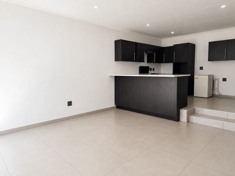 An open-plan living and kitchen area featuring dark cabinetry, a breakfast bar, tiled flooring, and recessed lighting in a clean, modern space.