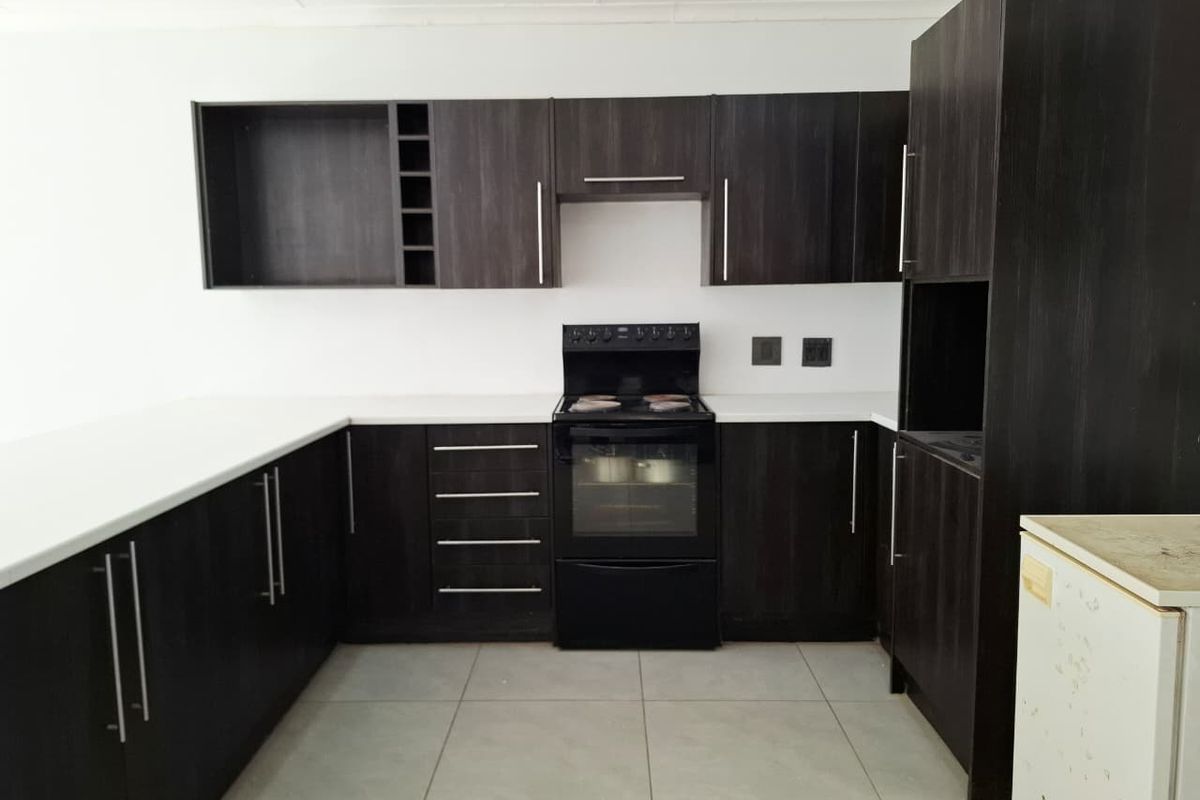 A clean, modern kitchen featuring dark wood cabinetry, white countertops, and a freestanding oven, offering a functional and well-maintained workspace.