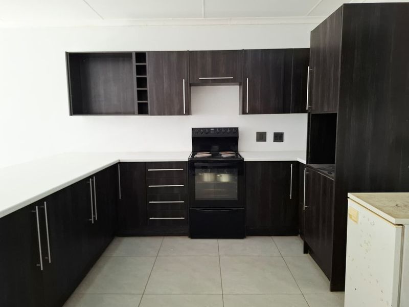 A clean, modern kitchen featuring dark wood cabinetry, white countertops, and a freestanding oven, offering a functional and well-maintained workspace.