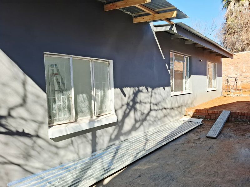 Rear exterior view of the property showing a freshly painted grey facade, steel windows with security bars, and ongoing construction work on the roof eaves.