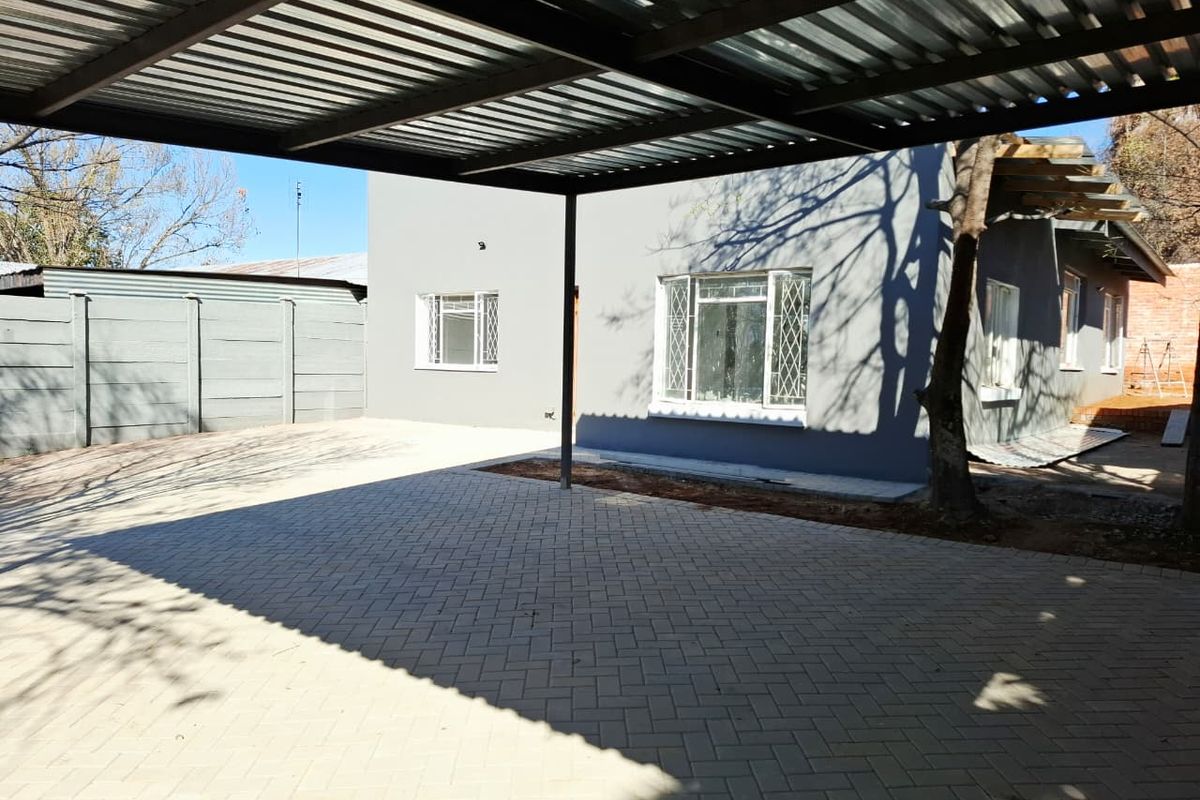 Rear exterior view featuring a covered carport, paved driveway, and precast boundary wall, with some unfinished landscaping areas visible.