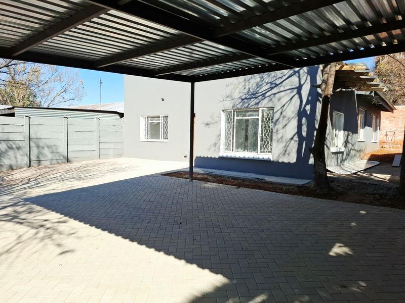 Rear exterior view featuring a covered carport, paved driveway, and precast boundary wall, with some unfinished landscaping areas visible.