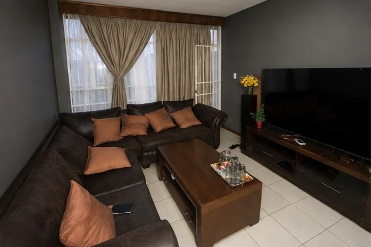 A living room featuring tiled flooring and a sliding door with an integrated security gate, providing access to the exterior.