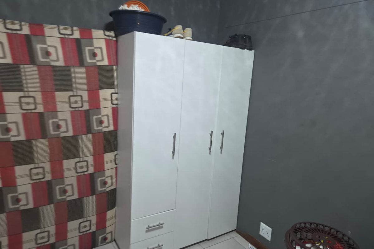 A bedroom featuring a white built-in wardrobe with drawers and tiled flooring, set against a dark grey wall with patterned accent wallpaper.