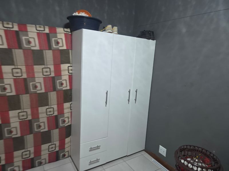 A bedroom featuring a white built-in wardrobe with drawers and tiled flooring, set against a dark grey wall with patterned accent wallpaper.