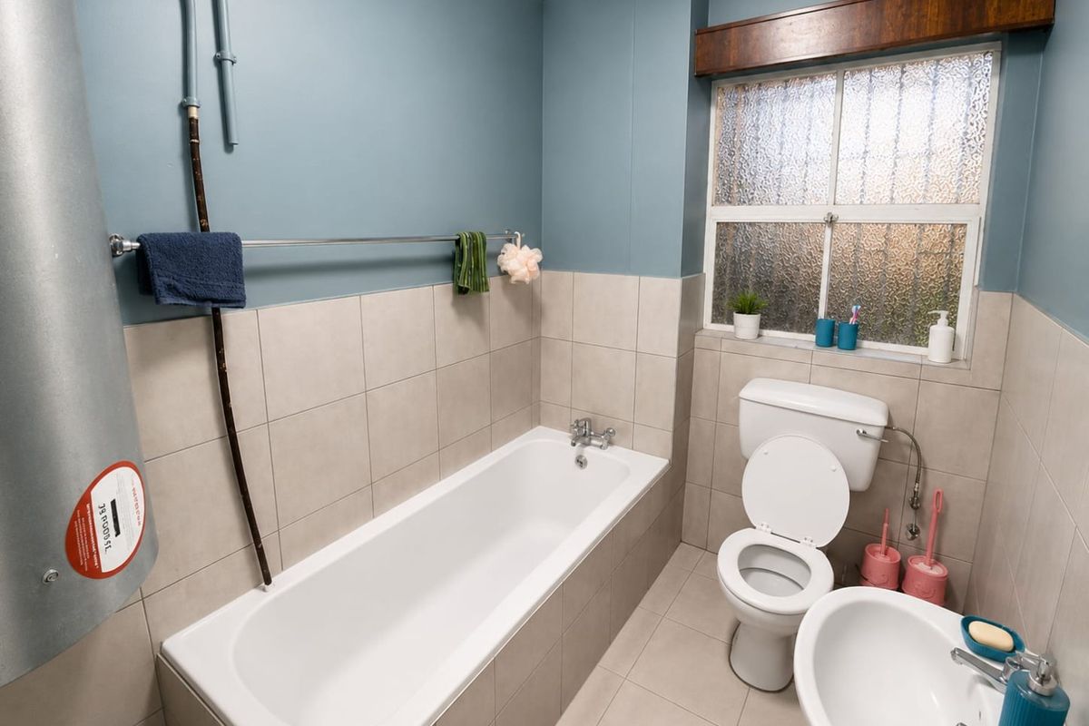 A functional bathroom featuring a bathtub, toilet, and washbasin with neutral wall and floor tiling and an obscured glass window for privacy.