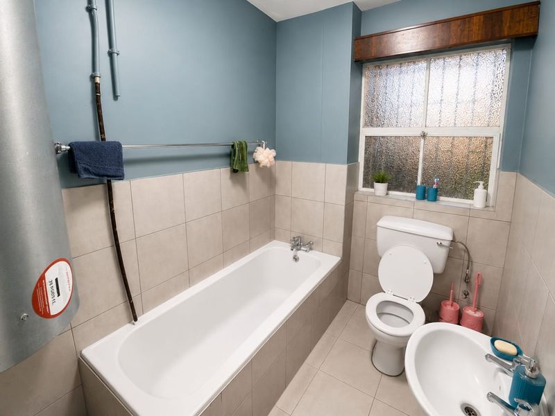 A functional bathroom featuring a bathtub, toilet, and washbasin with neutral wall and floor tiling and an obscured glass window for privacy.