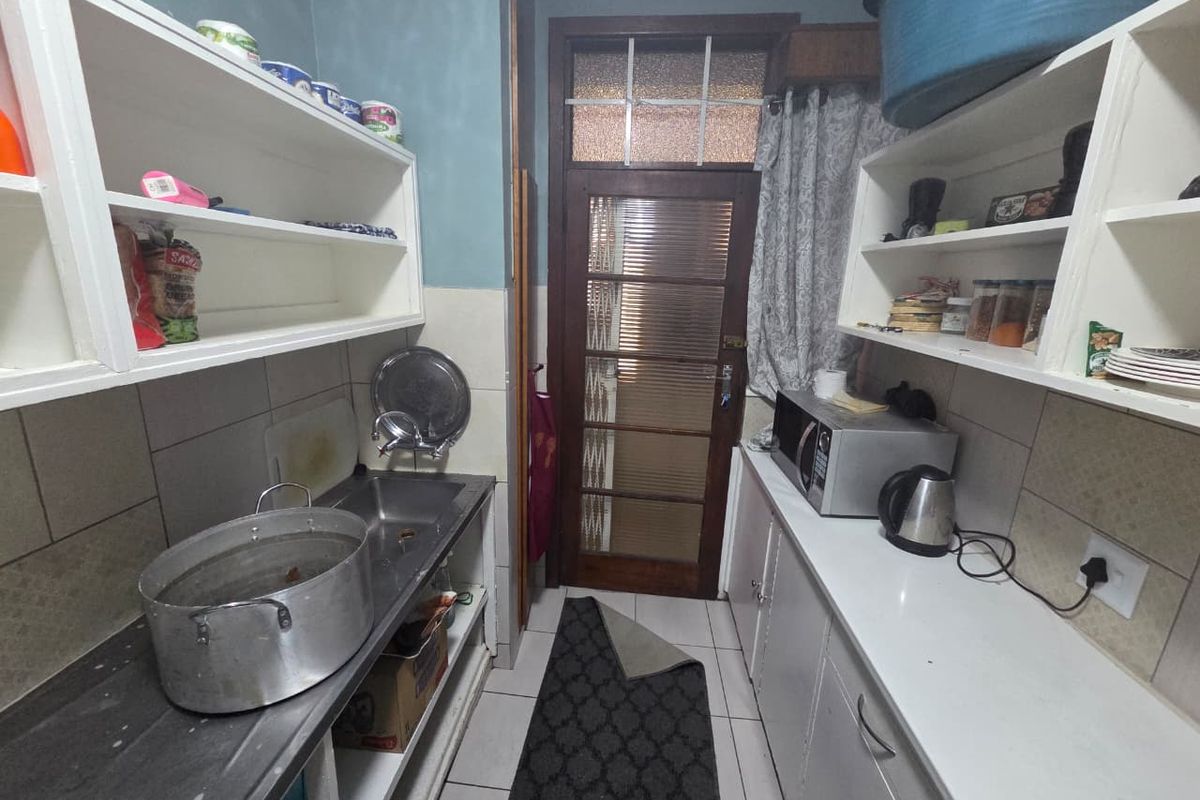 A functional scullery area featuring built-in shelving, a stainless steel sink, and tiled finishes, providing additional prep and storage space.