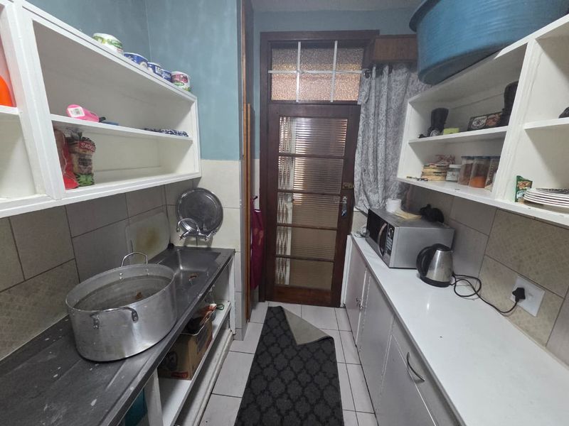 A functional scullery area featuring built-in shelving, a stainless steel sink, and tiled finishes, providing additional prep and storage space.