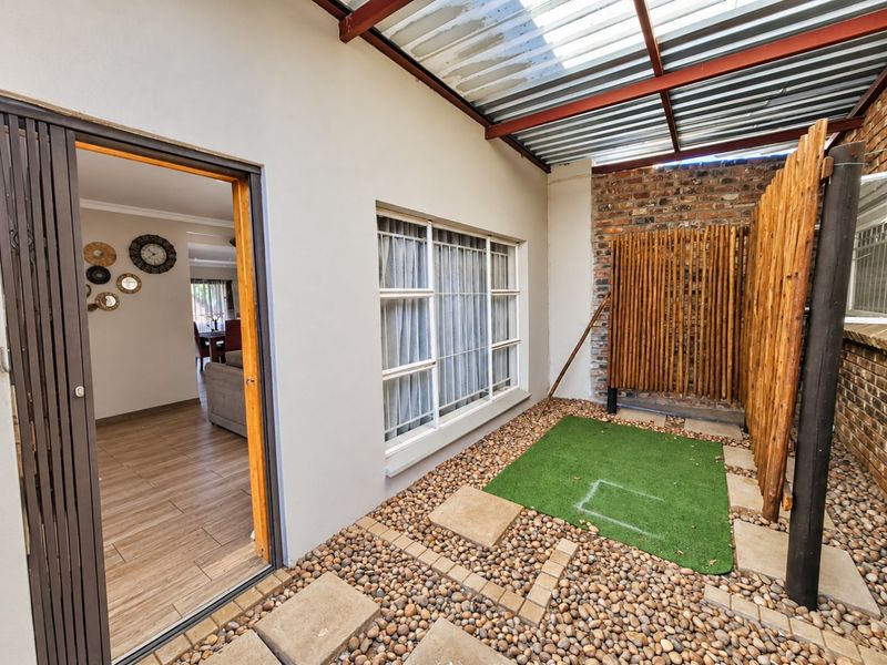 A covered outdoor patio area featuring a mix of pebble and artificial grass flooring, exposed brickwork, and a timber privacy screen.