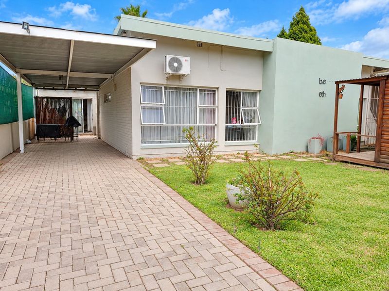 Front exterior view featuring a paved driveway, covered carport, well-maintained lawn, and a single-story building facade with aluminium windows and an external air conditioning unit.
