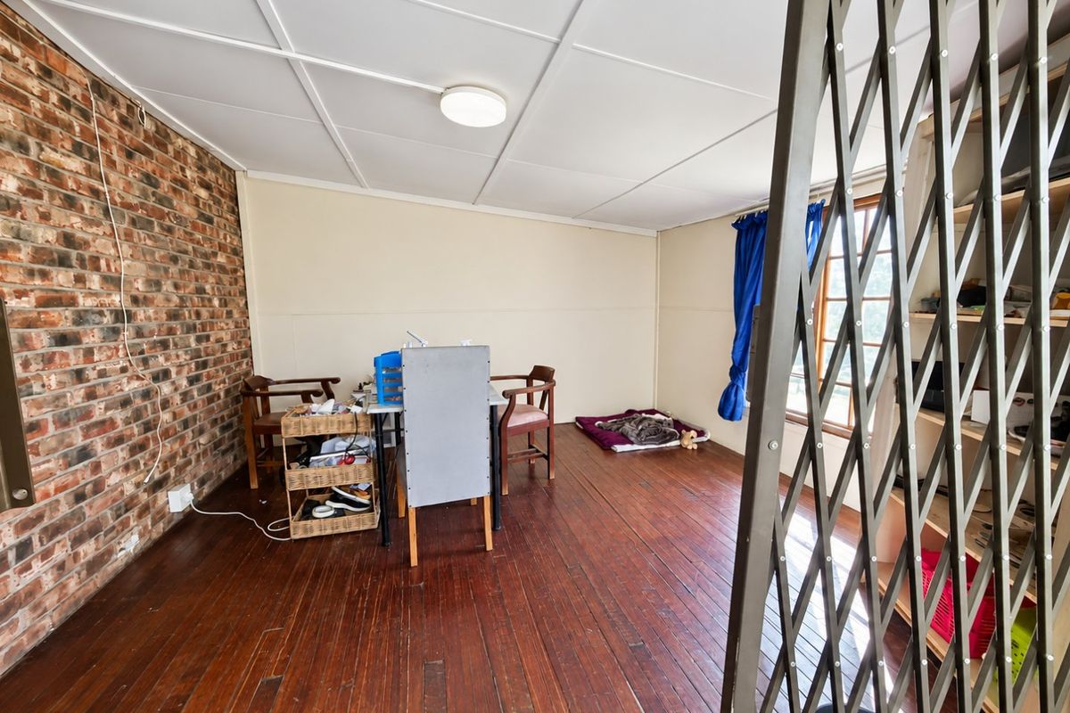 Living area featuring exposed brick wall, timber flooring, and a security gate, offering a rustic aesthetic with potential for modernization.