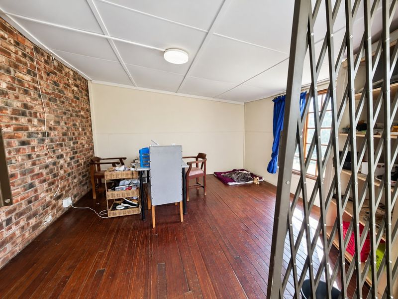 Living area featuring exposed brick wall, timber flooring, and a security gate, offering a rustic aesthetic with potential for modernization.