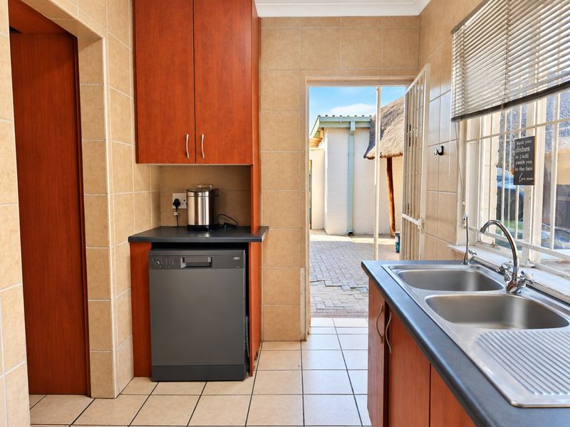 Functional scullery area featuring double stainless steel sink, laminate countertops, built-in cabinetry, and direct access to the rear exterior courtyard.