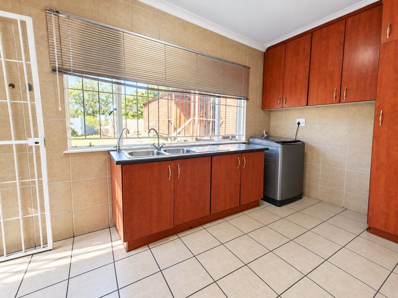Functional laundry room featuring tiled walls and floors, double sink, and ample wooden cabinetry for storage.