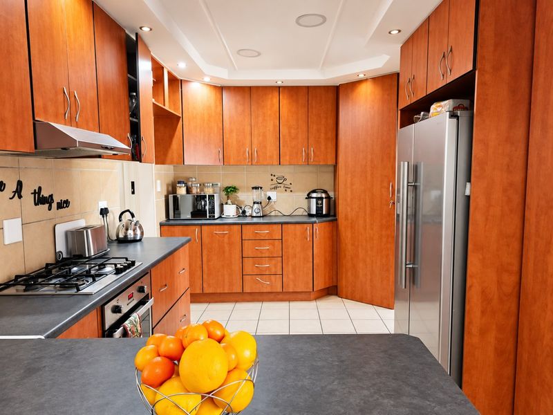 A functional kitchen featuring warm-toned wooden cabinetry, dark laminate countertops, a gas hob, built-in oven, and tiled flooring with recessed lighting.