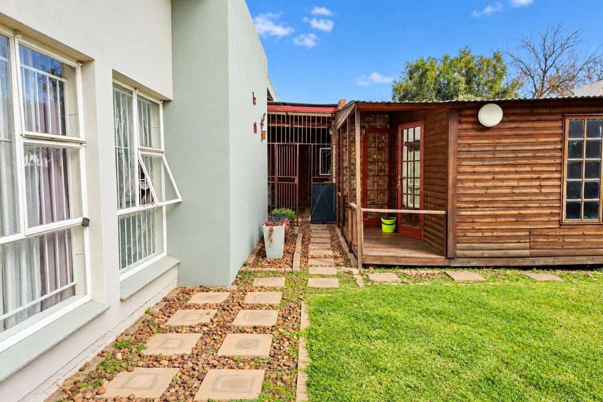 Rear exterior view featuring a timber-clad structure with a small deck, adjacent to a paved walkway and lawn area.