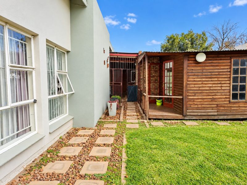 Rear exterior view featuring a timber-clad structure with a small deck, adjacent to a paved walkway and lawn area.