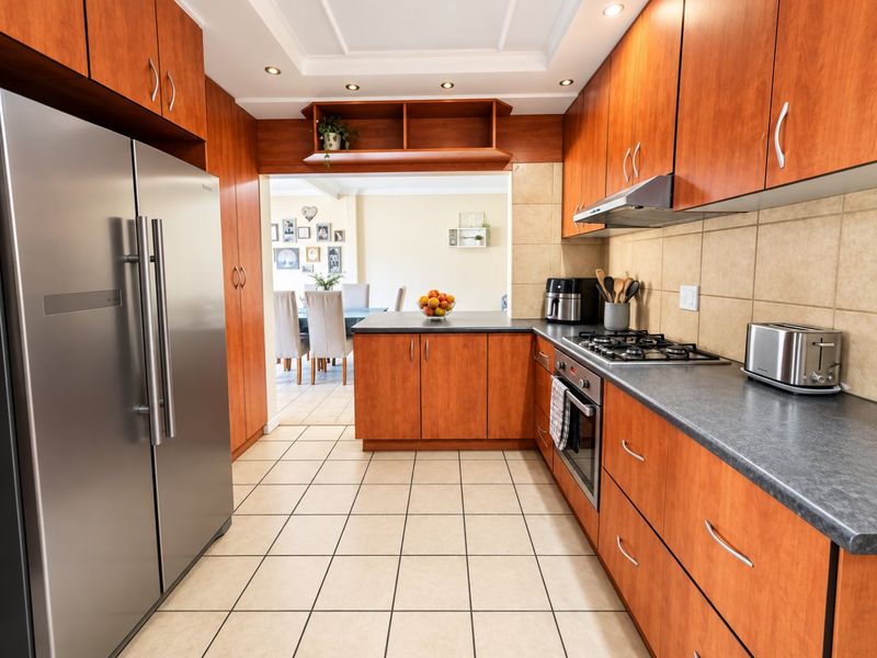 A functional kitchen featuring warm-toned wooden cabinetry, dark laminate countertops, a gas hob, and tiled flooring, with an open-plan flow to the dining area.