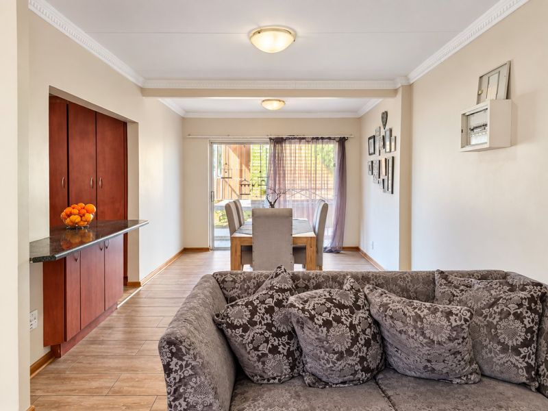 Open-plan living and dining area featuring tiled flooring, crown molding, and built-in cabinetry with a granite countertop, leading to a rear patio.