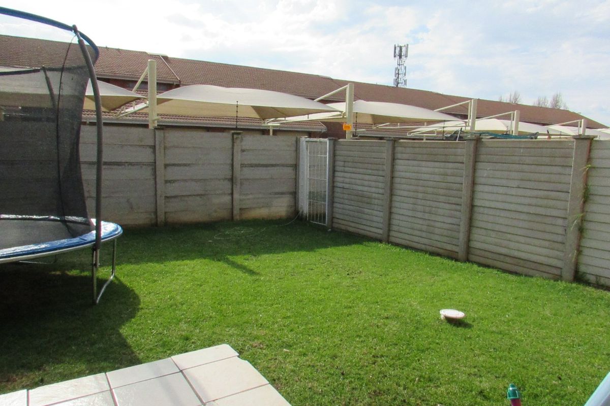 A private rear garden featuring a lawn, tiled patio area, and secure precast concrete boundary walling with a pedestrian gate.