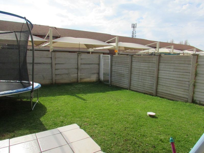 A private rear garden featuring a lawn, tiled patio area, and secure precast concrete boundary walling with a pedestrian gate.