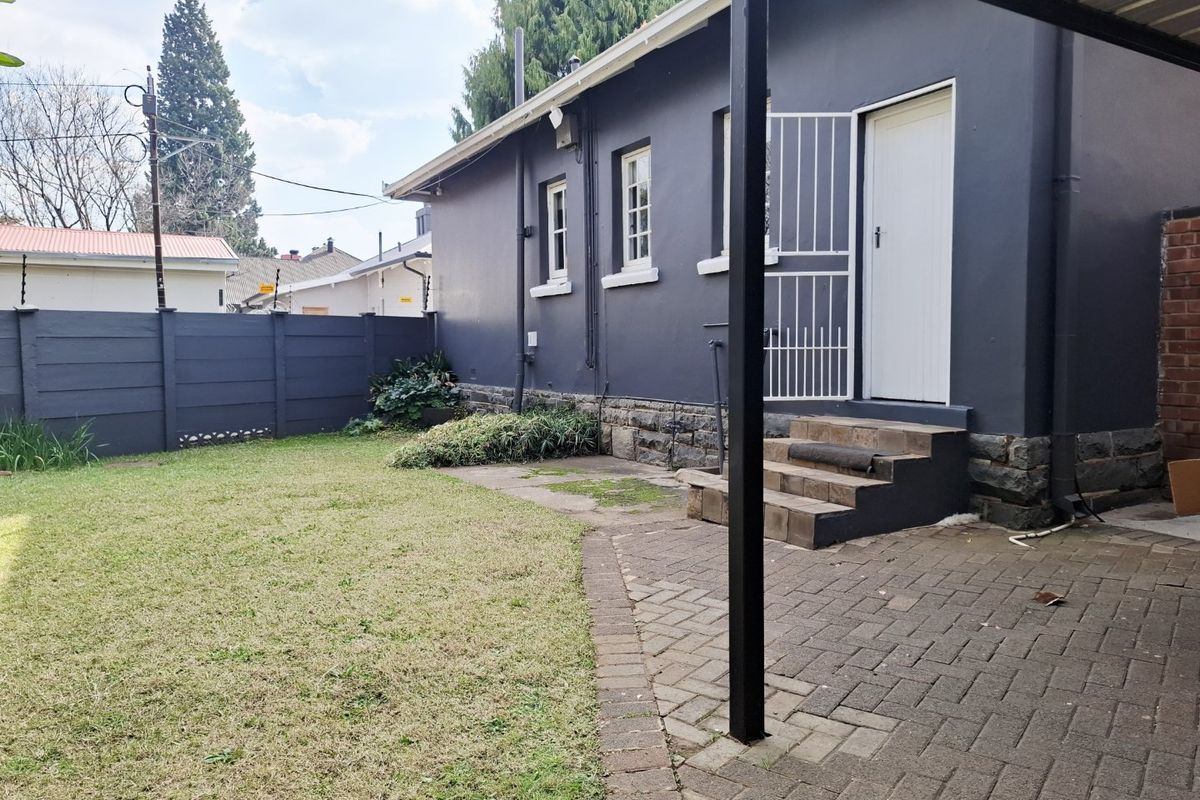 Rear exterior view featuring a paved patio area, stone foundation detailing, and a secure entrance with a security gate leading to the garden.