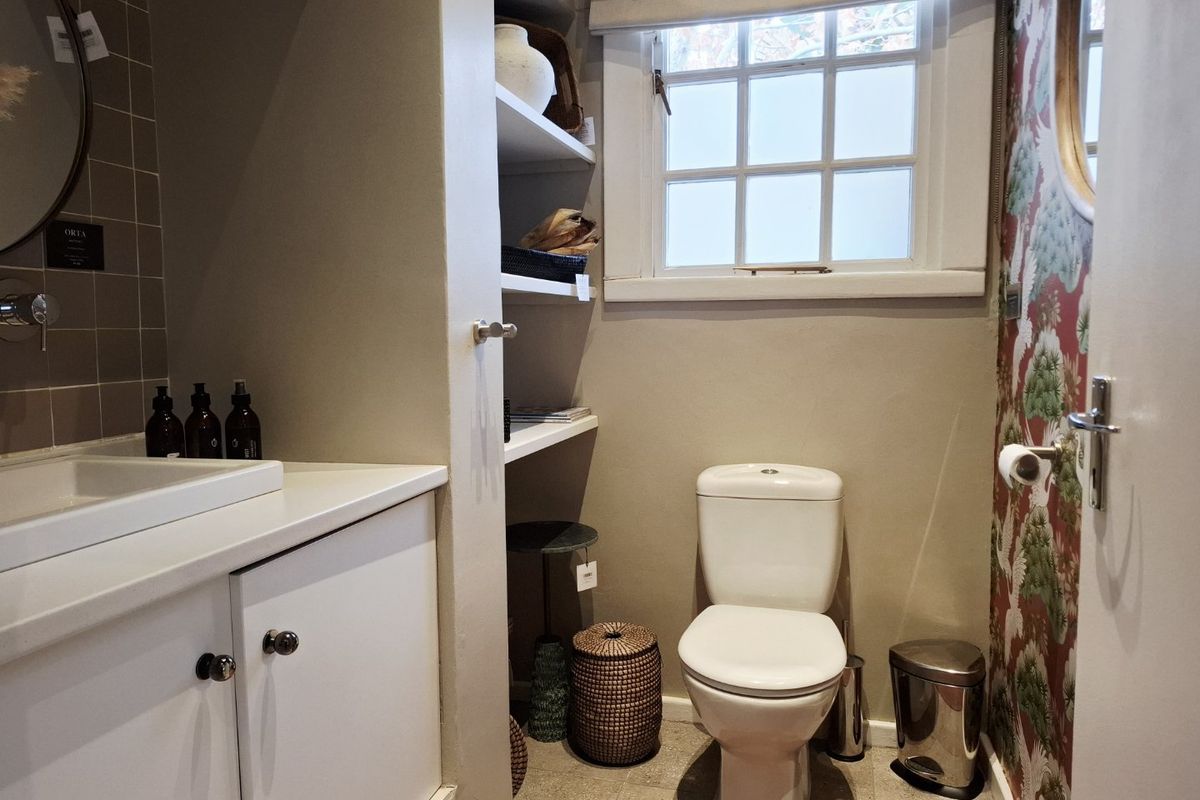 A well-maintained bathroom featuring a built-in vanity with basin, wall-mounted tapware, built-in shelving, and a toilet, finished with decorative wallpaper.