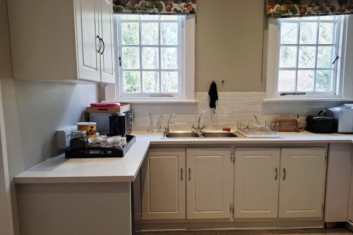 A functional kitchen area featuring white cabinetry, a double basin sink, subway tile backsplash, and classic sash windows providing natural light.