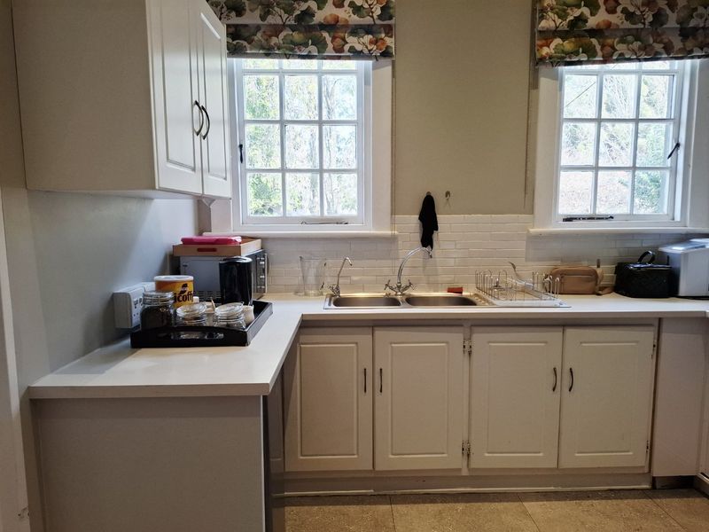 A functional kitchen area featuring white cabinetry, a double basin sink, subway tile backsplash, and classic sash windows providing natural light.