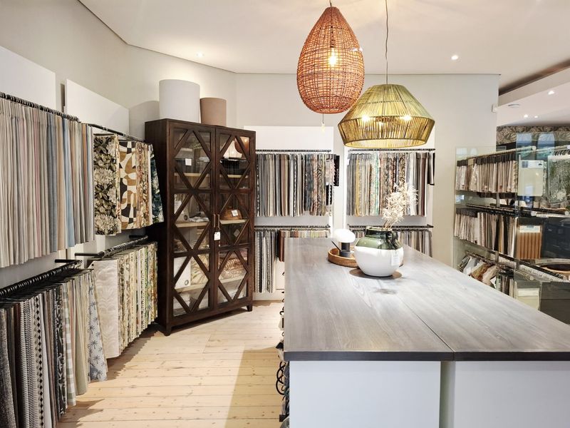 A well-maintained commercial showroom space featuring extensive built-in fabric sample display racks, hardwood flooring, and modern pendant lighting.