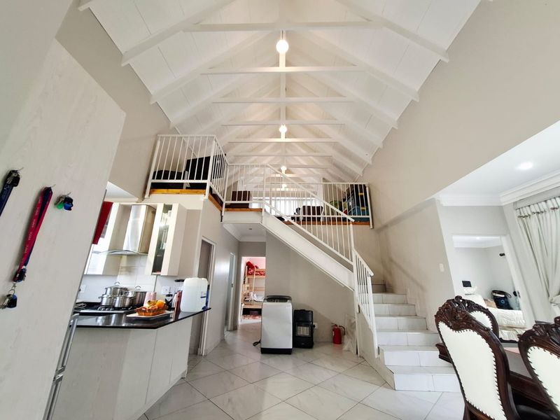 Spacious open-plan living area featuring a high vaulted ceiling with exposed rafters, a mezzanine level, and a modern kitchen with stone countertops.