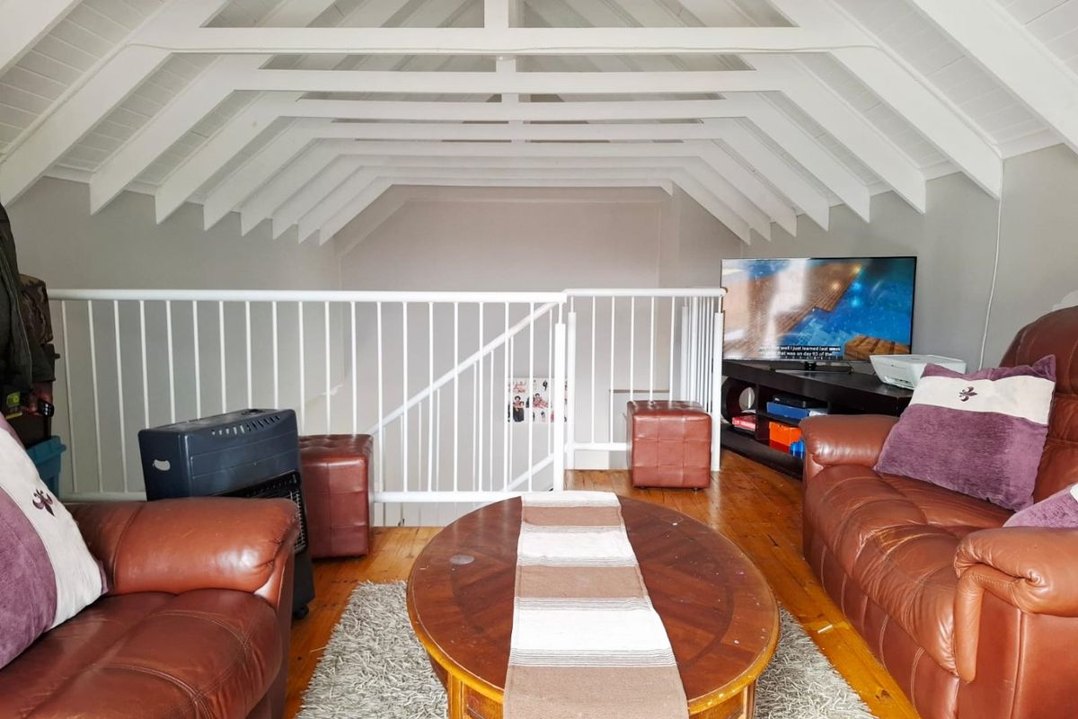 A cozy loft-style living area featuring a vaulted ceiling with exposed white rafters, timber flooring, and a protective metal balustrade overlooking the lower level.