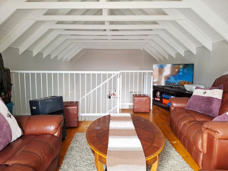 A cozy loft-style living area featuring a vaulted ceiling with exposed white rafters, timber flooring, and a protective metal balustrade overlooking the lower level.
