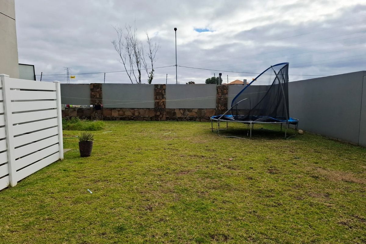 A private rear garden featuring a lawn area enclosed by a combination of stone masonry pillars and perimeter walls.