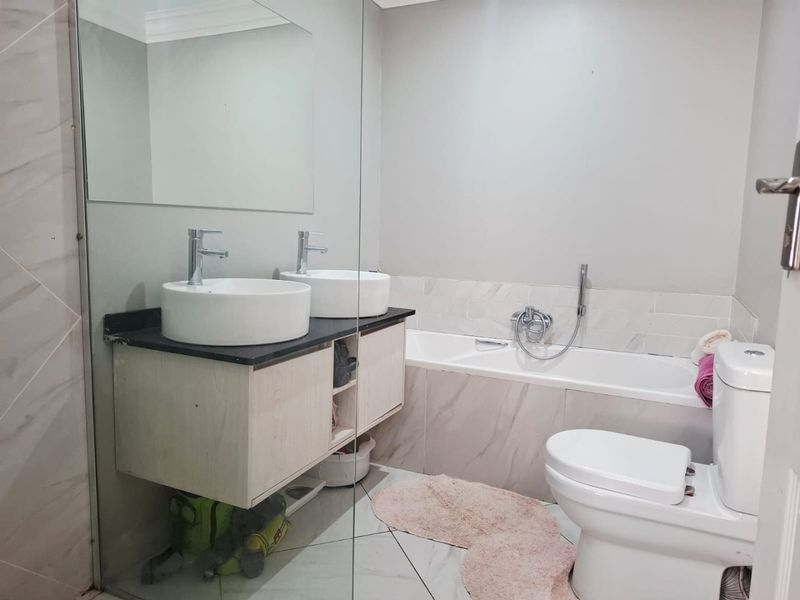 Modern bathroom featuring a double vanity with vessel sinks, a built-in bathtub with handheld shower mixer, and contemporary tiled finishes.