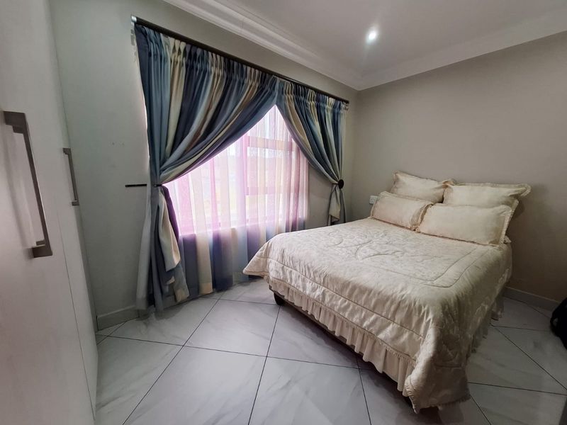 A well-maintained bedroom featuring tiled flooring, built-in wardrobe storage, and recessed ceiling lighting with decorative coving.