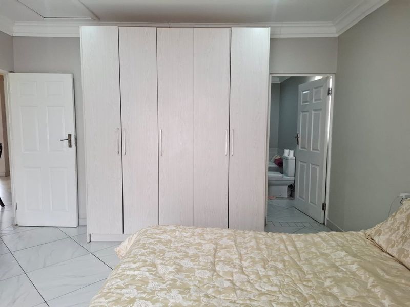 A bedroom featuring light-toned tiled flooring, built-in wardrobes, and direct access to an en-suite bathroom.