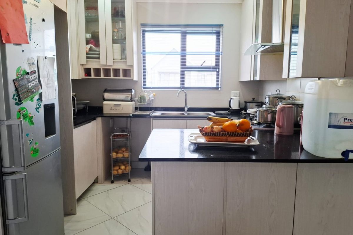 A functional kitchen featuring light wood-finish cabinetry, dark granite countertops, tiled flooring, and a stainless steel sink with a window view.