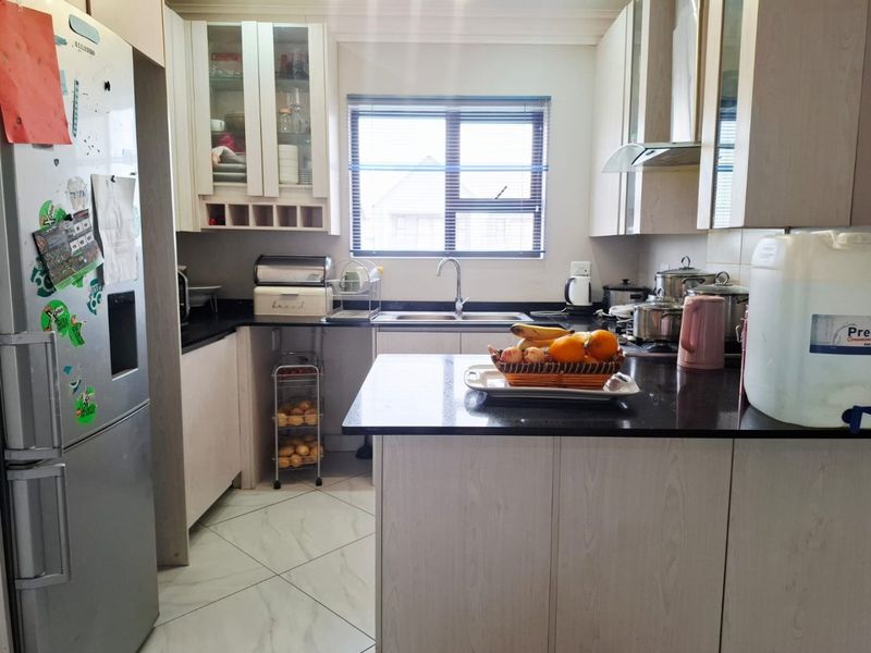 A functional kitchen featuring light wood-finish cabinetry, dark granite countertops, tiled flooring, and a stainless steel sink with a window view.