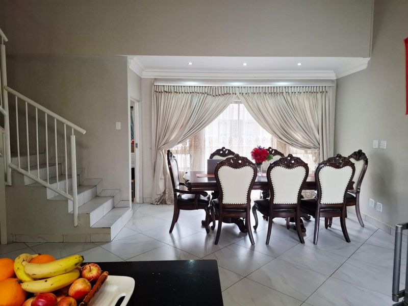 A well-lit dining area featuring tiled flooring, crown molding, and a staircase with a metal railing, leading to a large window with curtain treatments.