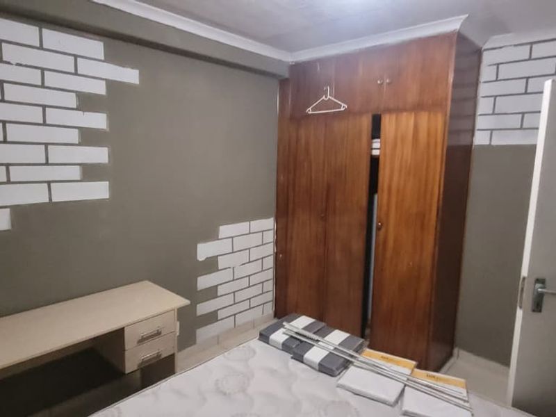 A bedroom featuring a built-in wooden wardrobe and decorative wall detailing, requiring cosmetic updates to improve the overall finish and aesthetic appeal.