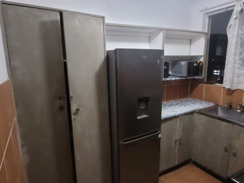 A compact kitchen featuring dated cabinetry, tiled backsplash, and a stainless steel sink, offering potential for modernization and improved layout efficiency.