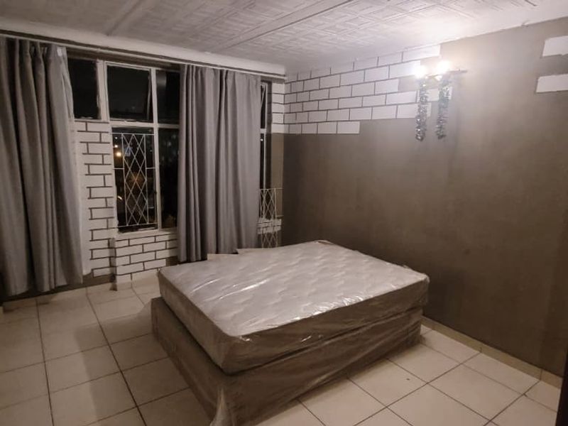 A bedroom featuring tiled flooring and security bars on the window, currently undergoing wall renovations with unfinished plastering.