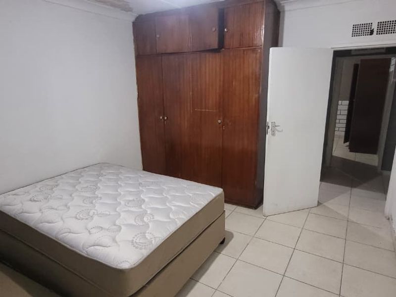 A bedroom featuring built-in wooden cupboards and tiled flooring, requiring cosmetic updates to the walls and ceiling.
