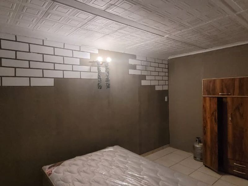 A bedroom featuring tiled flooring, textured ceiling tiles, and a wall sconce, currently undergoing wall finish updates.