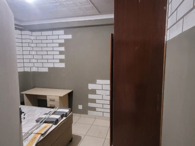 A bedroom featuring tiled flooring, a built-in cupboard, and textured ceiling tiles, currently requiring cosmetic updates to the wall finishes.