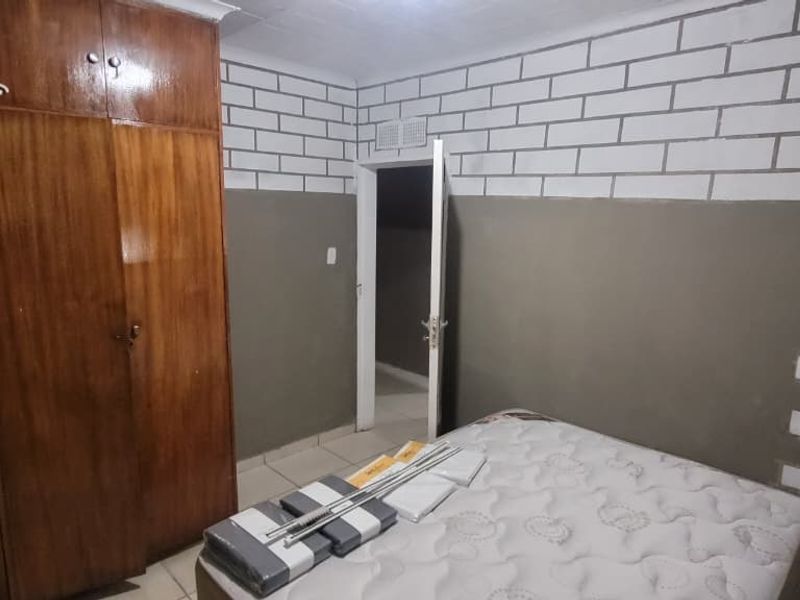 A bedroom featuring built-in wooden wardrobes, tiled flooring, and a two-tone wall finish with decorative brick-effect detailing.