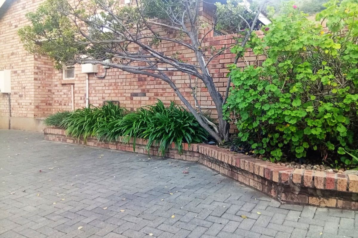 A rear exterior view of the townhouse featuring a brick paved courtyard area with a built-in brick retaining wall and established garden beds.